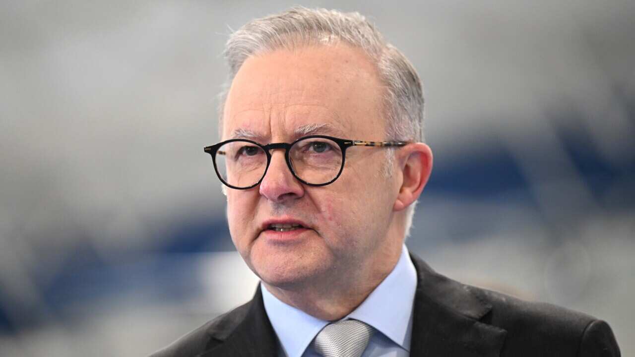 Anthony Albanese standing in front of a blurred white and blue background.
