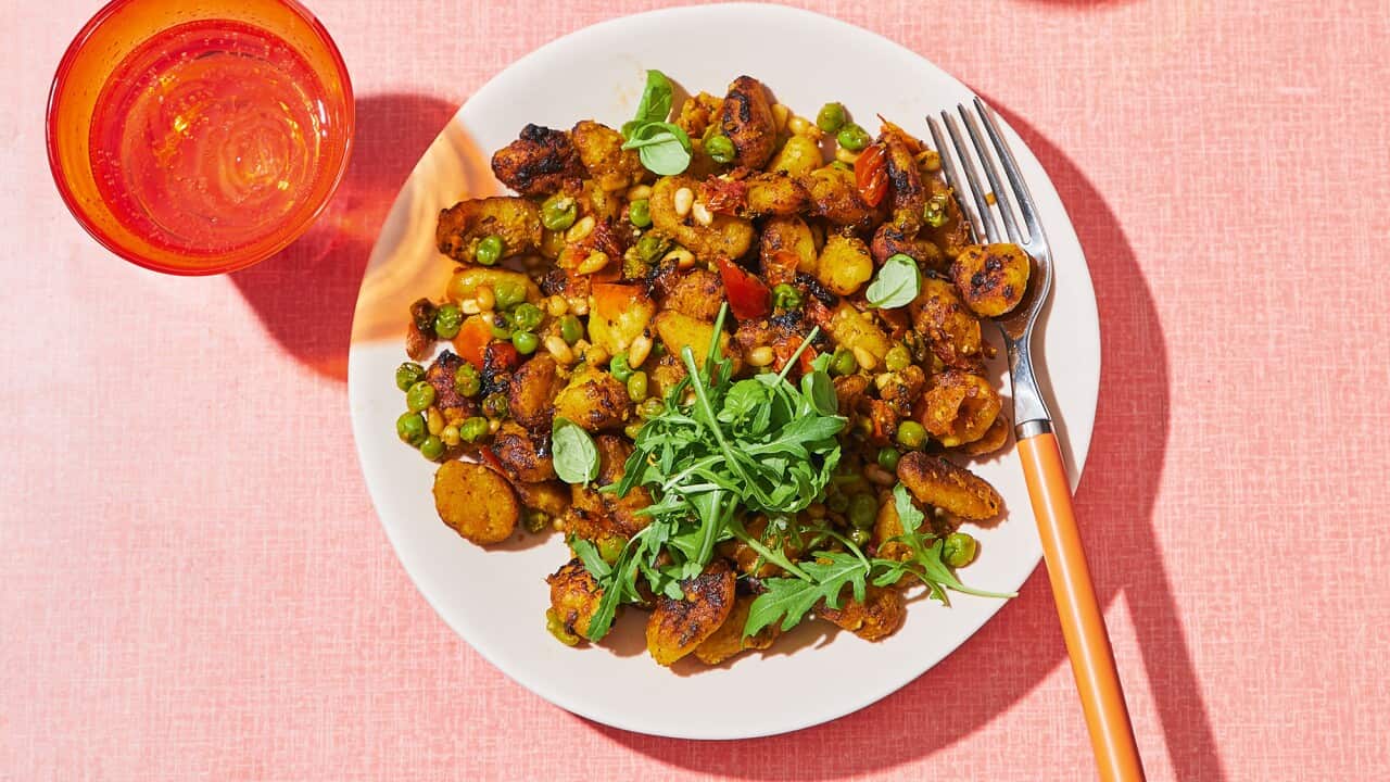 Seen from overhead, two plates with golden gnocchi sit on a blush-coloured tablecloth. Orange glasses sit alongside.