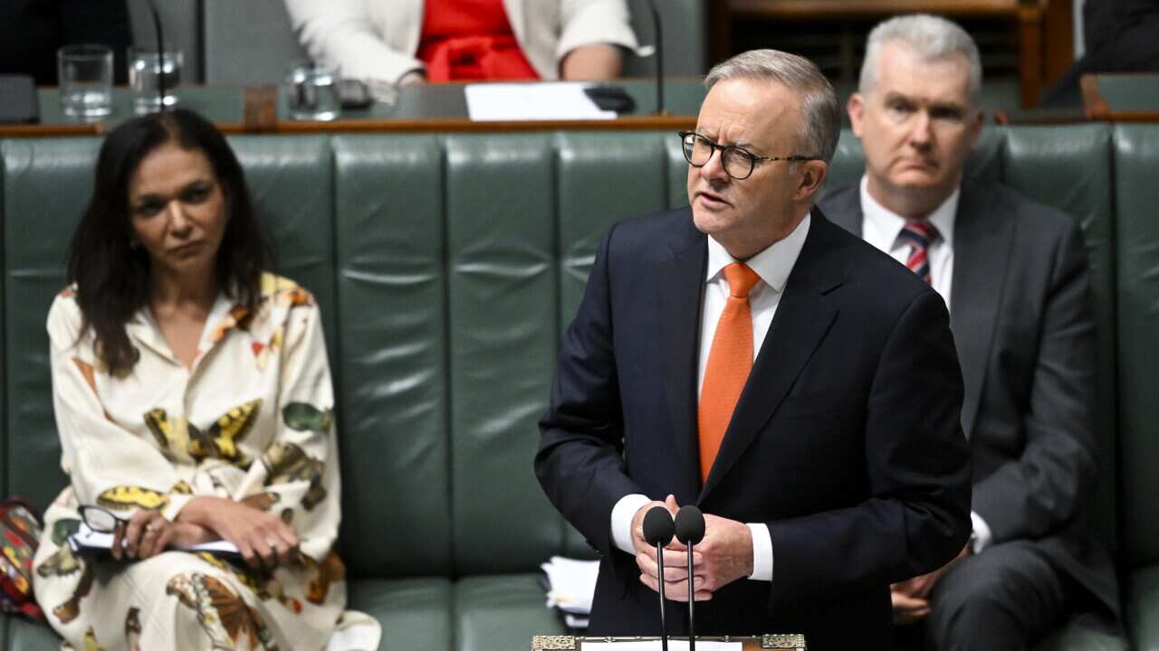 A man in a suit and orange tie speaks at a lecturn.