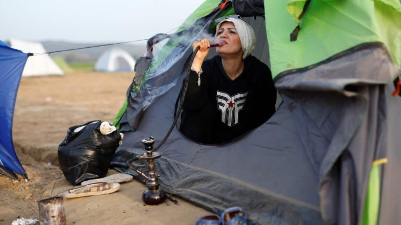 A migrant woman smokes as she sits in her tent at Idomeni, Greece