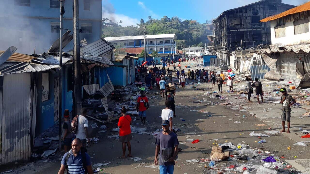 People gather as smoke rises from a burnt out building in Honiara's Chinatown on 26 November, 2021.