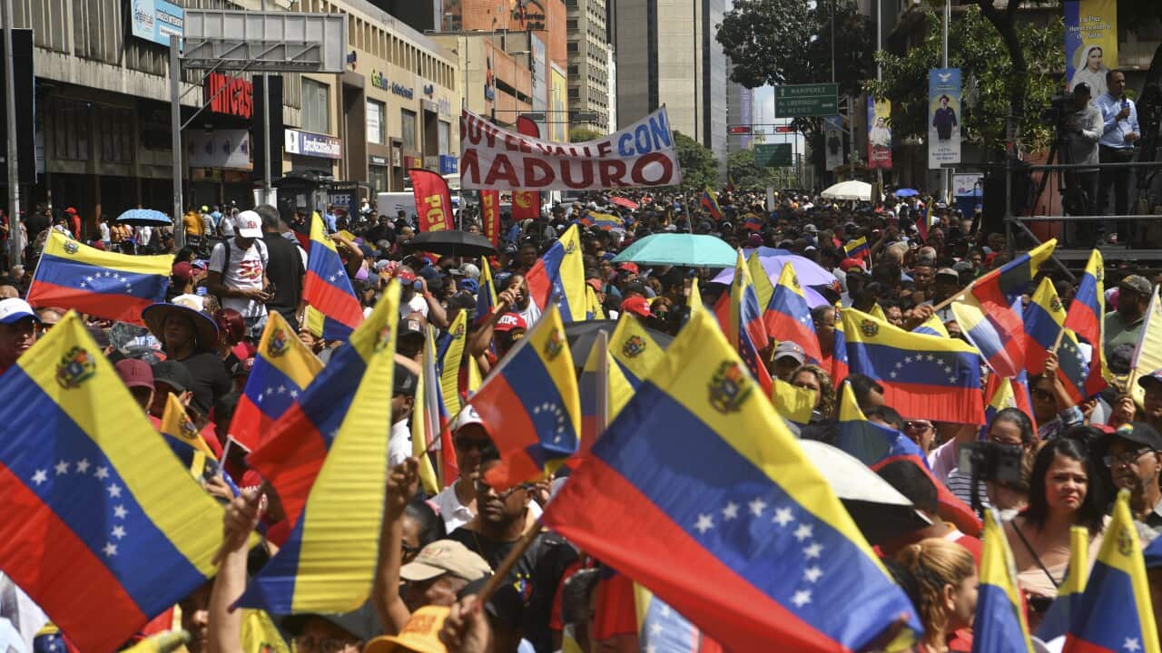 A large crowd of people walking down a street, waving Venezuelan flags.