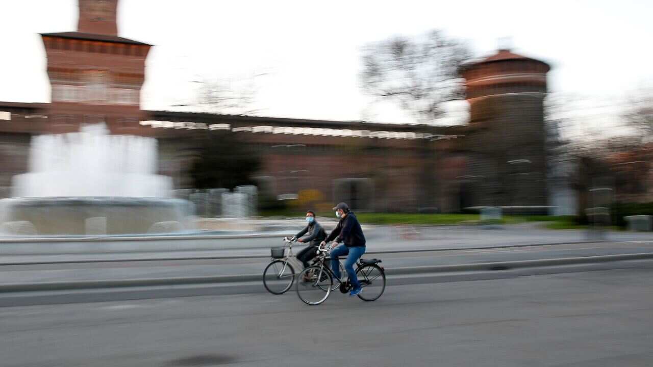 People wearing protective mask ride their bicycle at the Castello Sforzesco castle in Milan, Italy