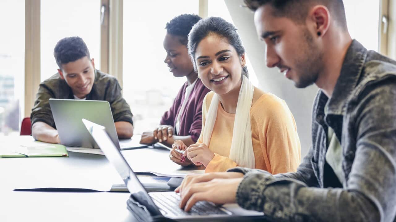 Young man using laptop with female student watching and smiling