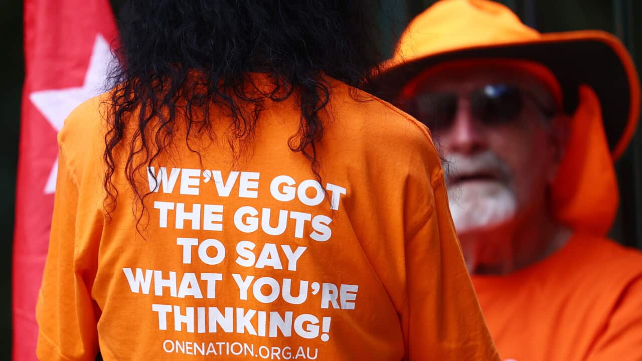One Nation members in orange shirts. A woman's back is towards the camera, with her shirt saying 'We've got the gut to say what you're thinking'