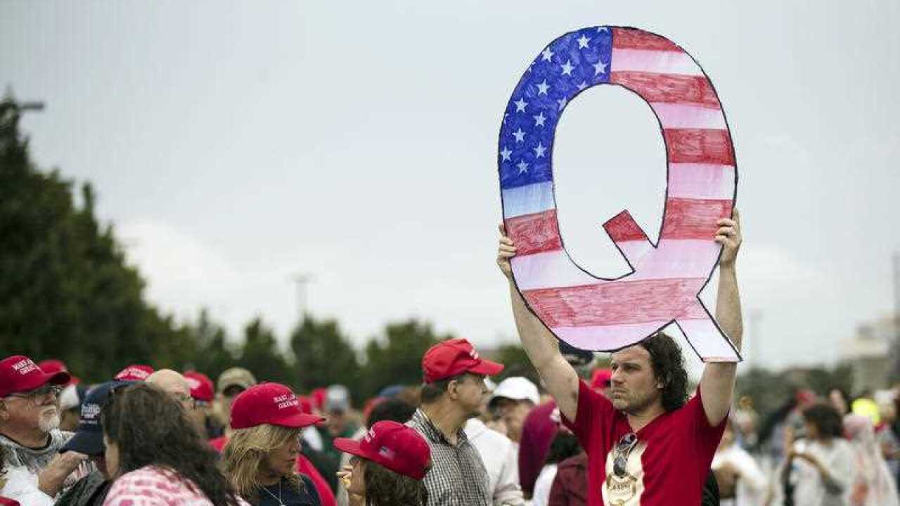 A protesters holds a Q sign waits in line with others to enter a campaign rally with President Donald Trump in 2018.