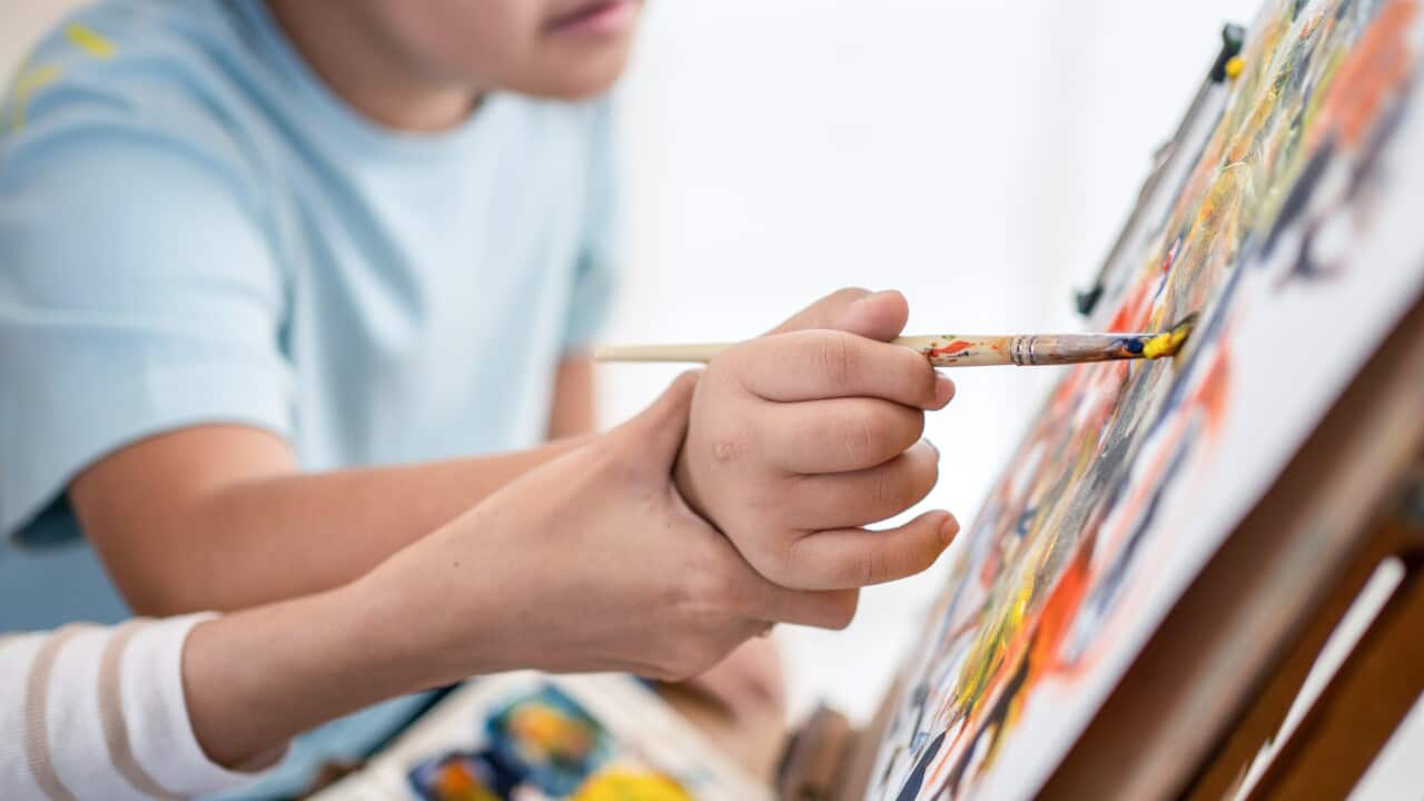 A young art teacher woman helps children with autism to paint on canvas.