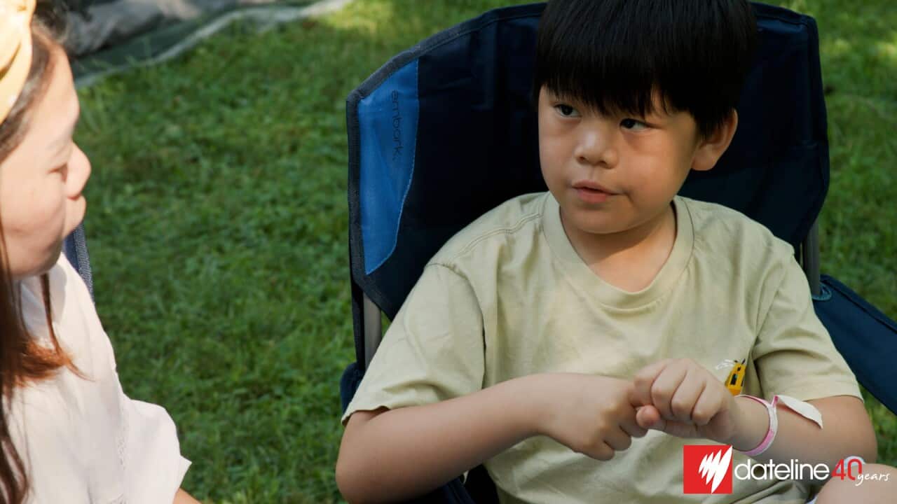 Asian American boy seated outdoors.