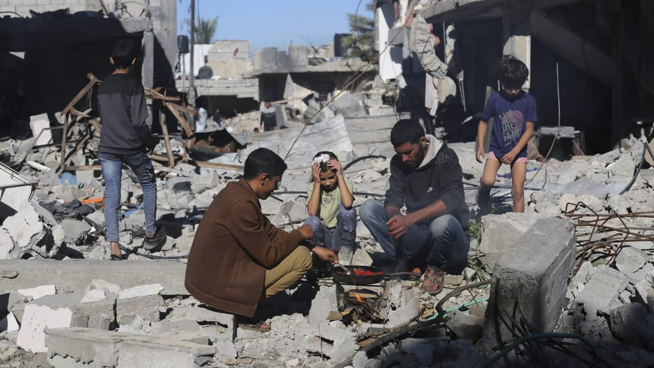 Four people squatting on the ground amid rubble