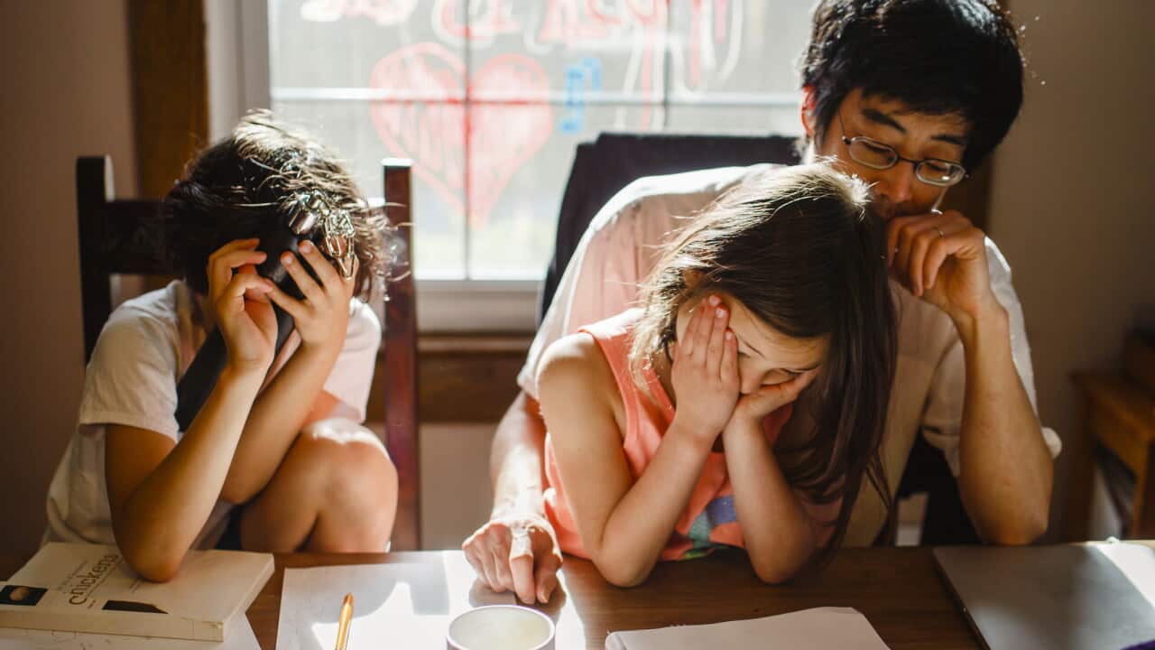 two unhappy children with head in hands sit with tired father at table