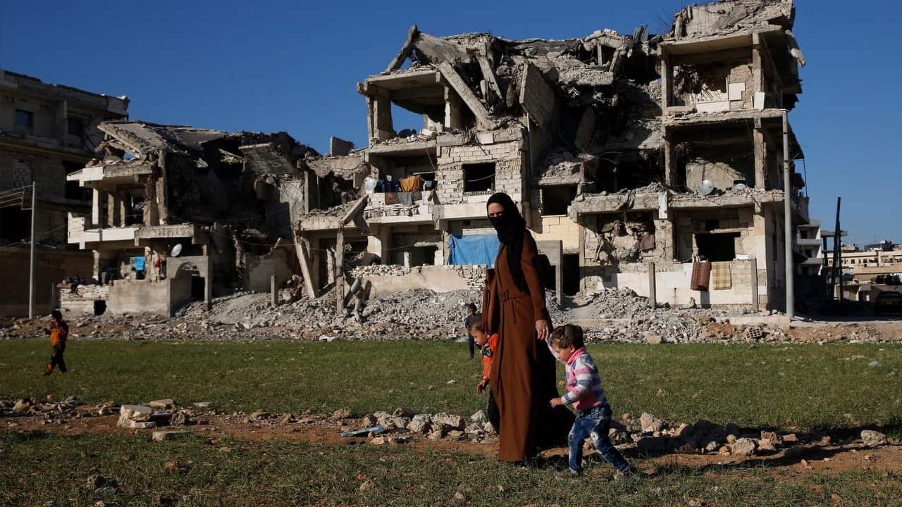 Syrian woman with her kids walks in front of buildings destroyed during fighting in Manbij.