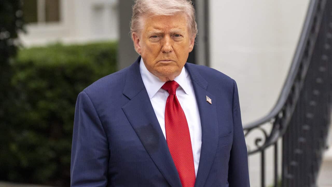 Trump sitting at his desk in the Oval Office at the White House wearing a navy suit and a red tie