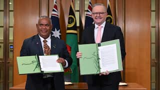 Jotham Napat and Anthony Albanese standing beside each other, in front of the national flags and holding a document.