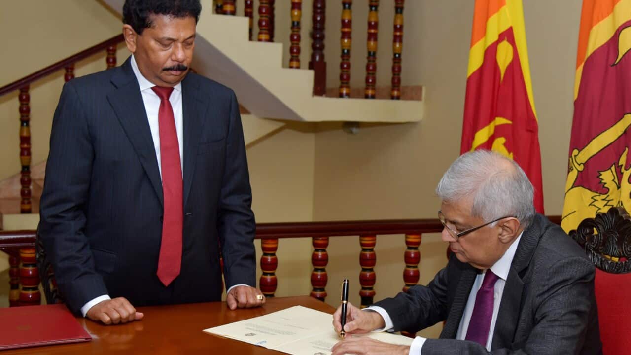 Sri Lankan Prime Minister Ranil Wickremesinghe sitting at a table (right) signing a document before Chief Justice Jayantha Jayasuriya (left).
