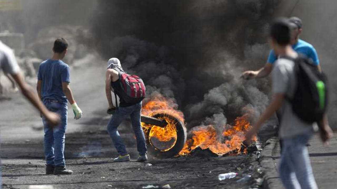 A Palestinian pushes burning tries during clashes with Israeli troops near Ramallah, West Bank, Tuesday, Oct. 13, 2015. (AAP)