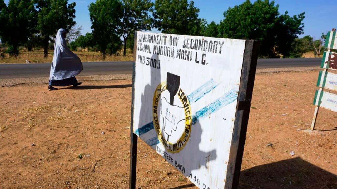 A veiled woman walks past a signpost of a secondary school in Katsina state, Nigeria on November 3, 2017