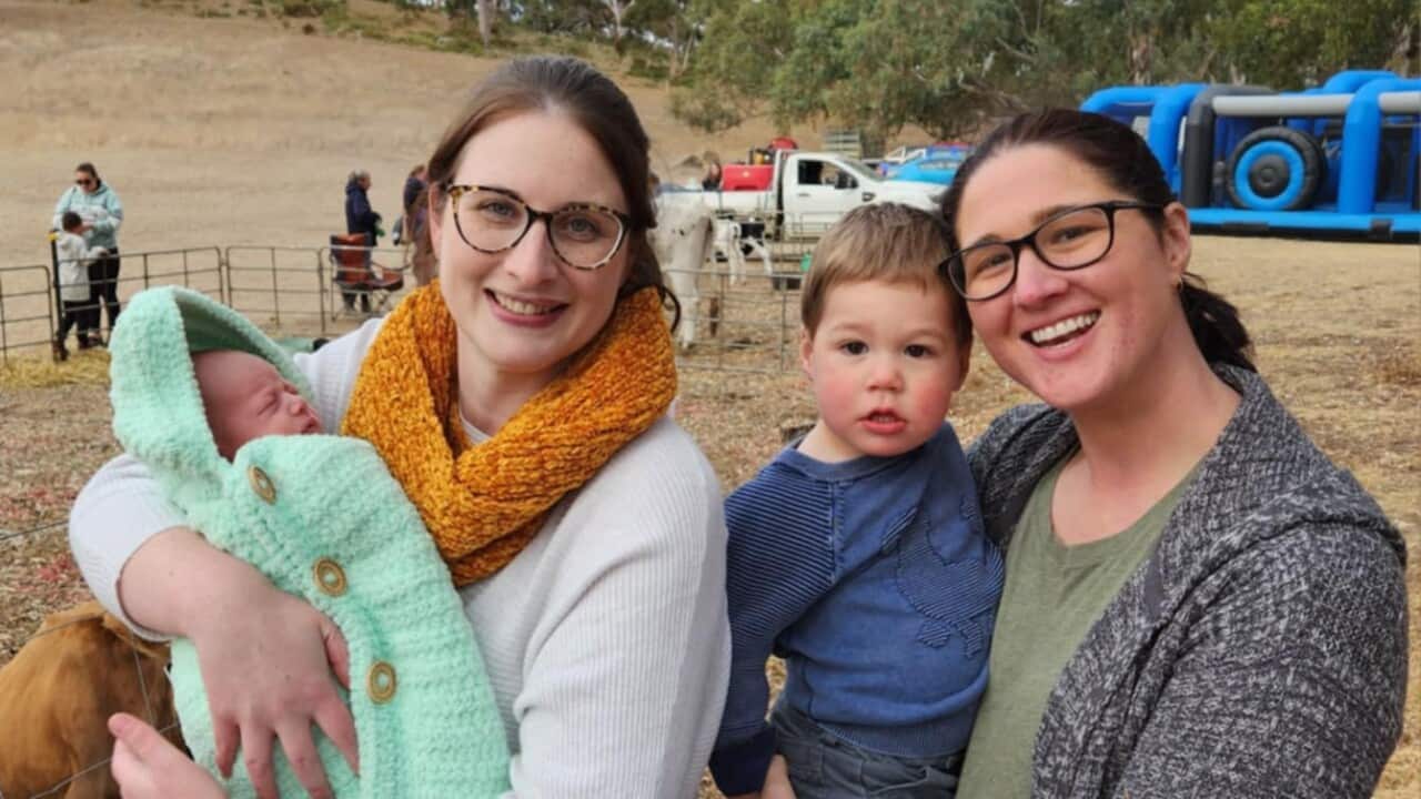 Two women smile while holding their two children.