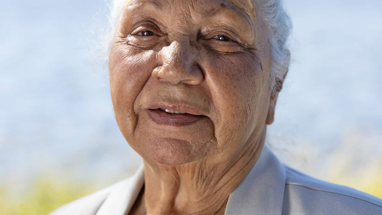 A portrait of a woman looking at the camera with water in the background.