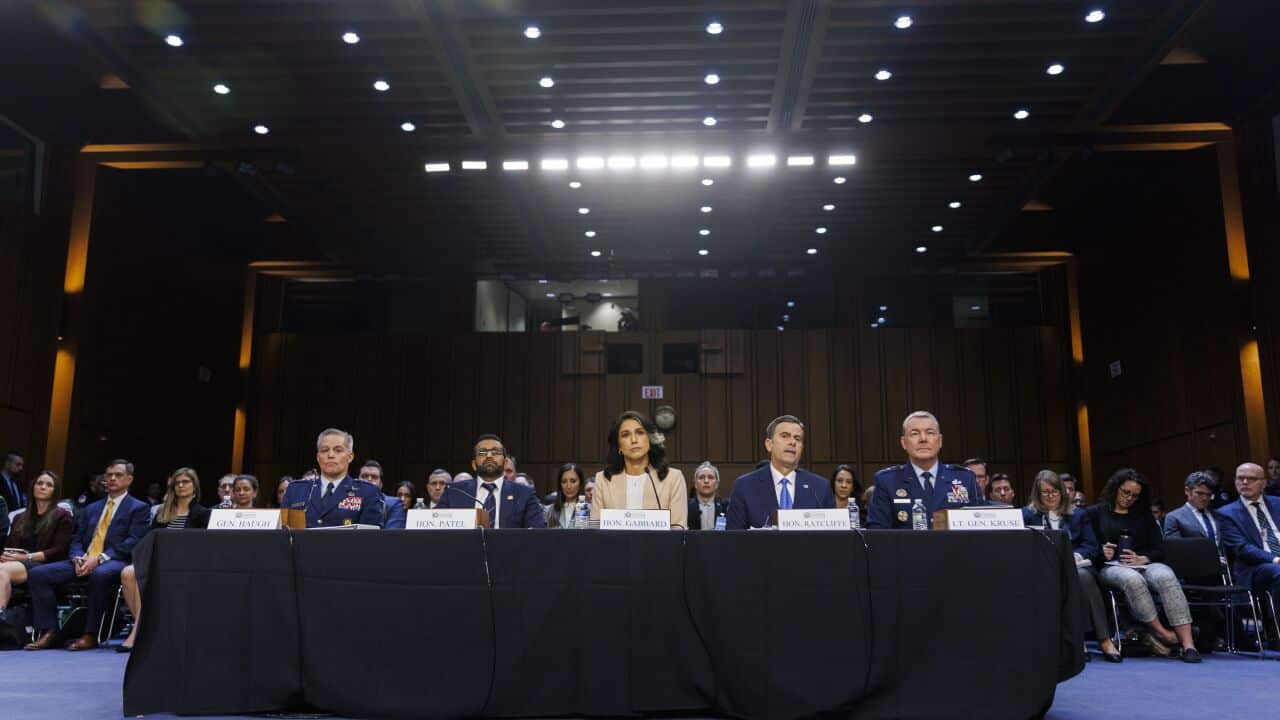 Five people sit at a table with name cards and microphones in large room full of people.