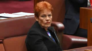 Pauline Hanson is sitting in Parliament wearing a black blazer and pouting.