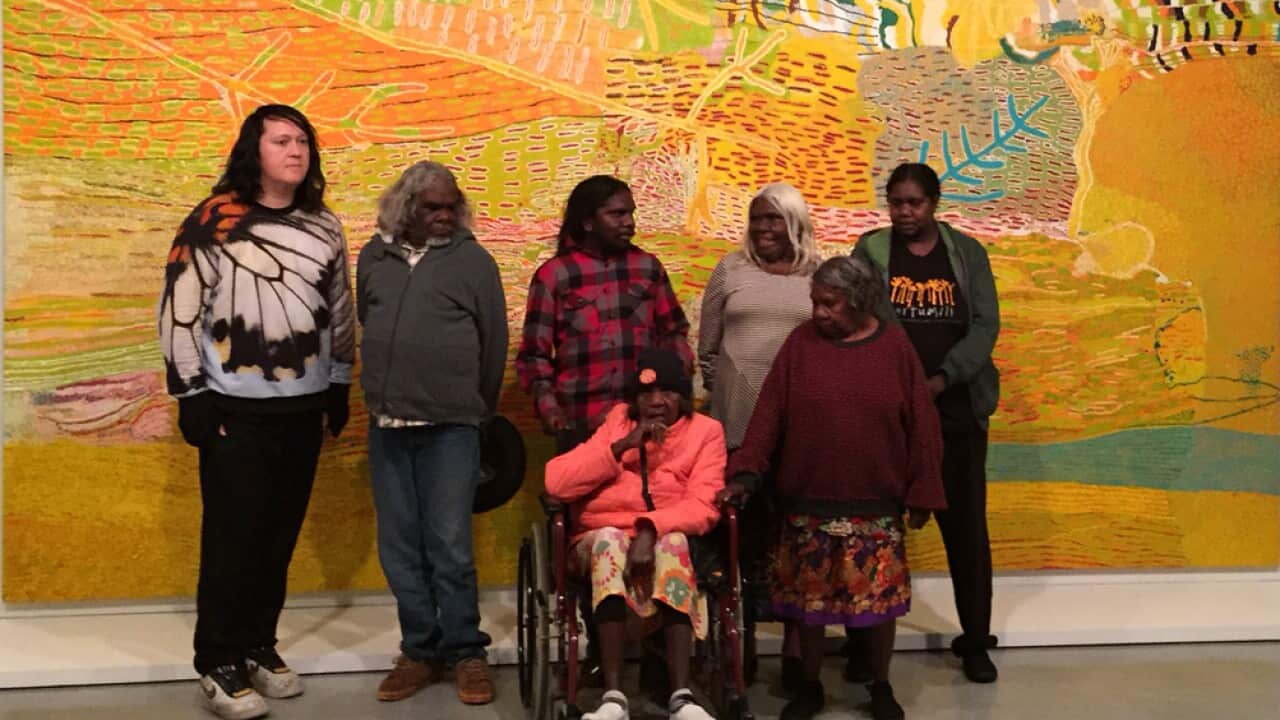 Martu artists in Parnngurr in the east Pilbara region of Western Australia stand with their work 'Kalyu' (SBS)