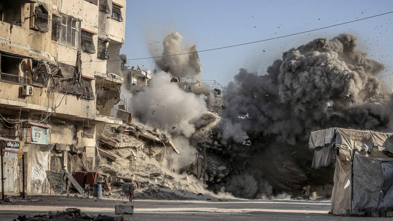 Debris and smoke rise from a concrete building hit during an airstrike in a city street.
