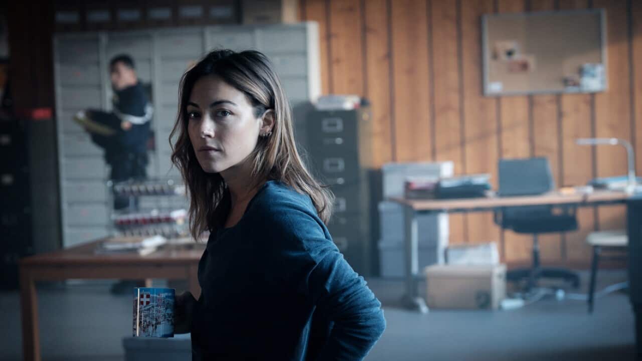 A woman stands in a police station holding a mug