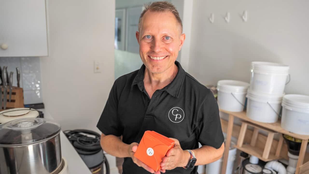 A man in a black t-shirt holds orange chocolate packets.