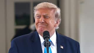 Trump wearing a suit and a blue tie, smiling.