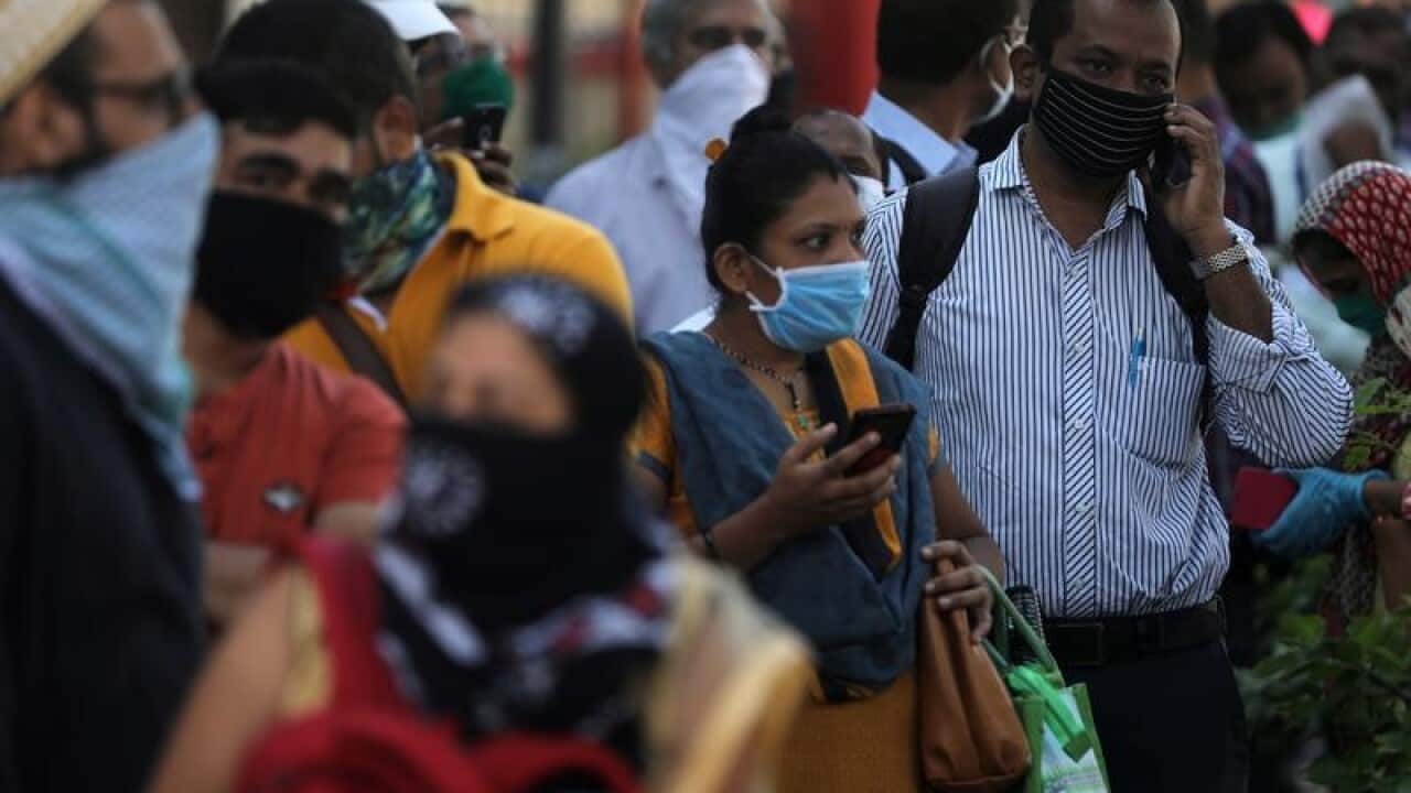 People wait in a queue to board a public bus in Mumbai
