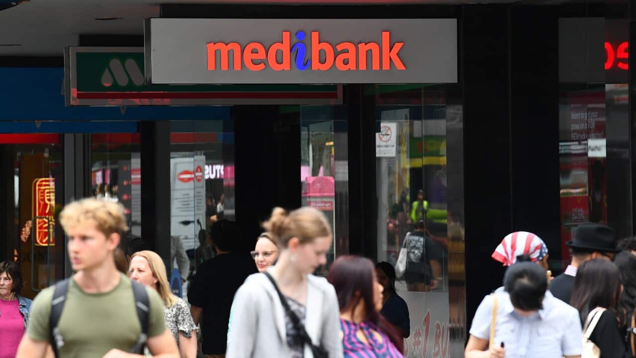 People walking along a street. A sign on a shopfront above them reads: "Medibank".