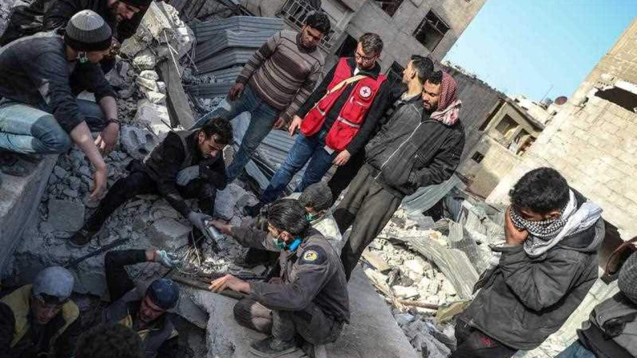 A volunteer with International Committee of the Red Cross observes Civil defense rescuers searching for a body of victim under a collapsed building