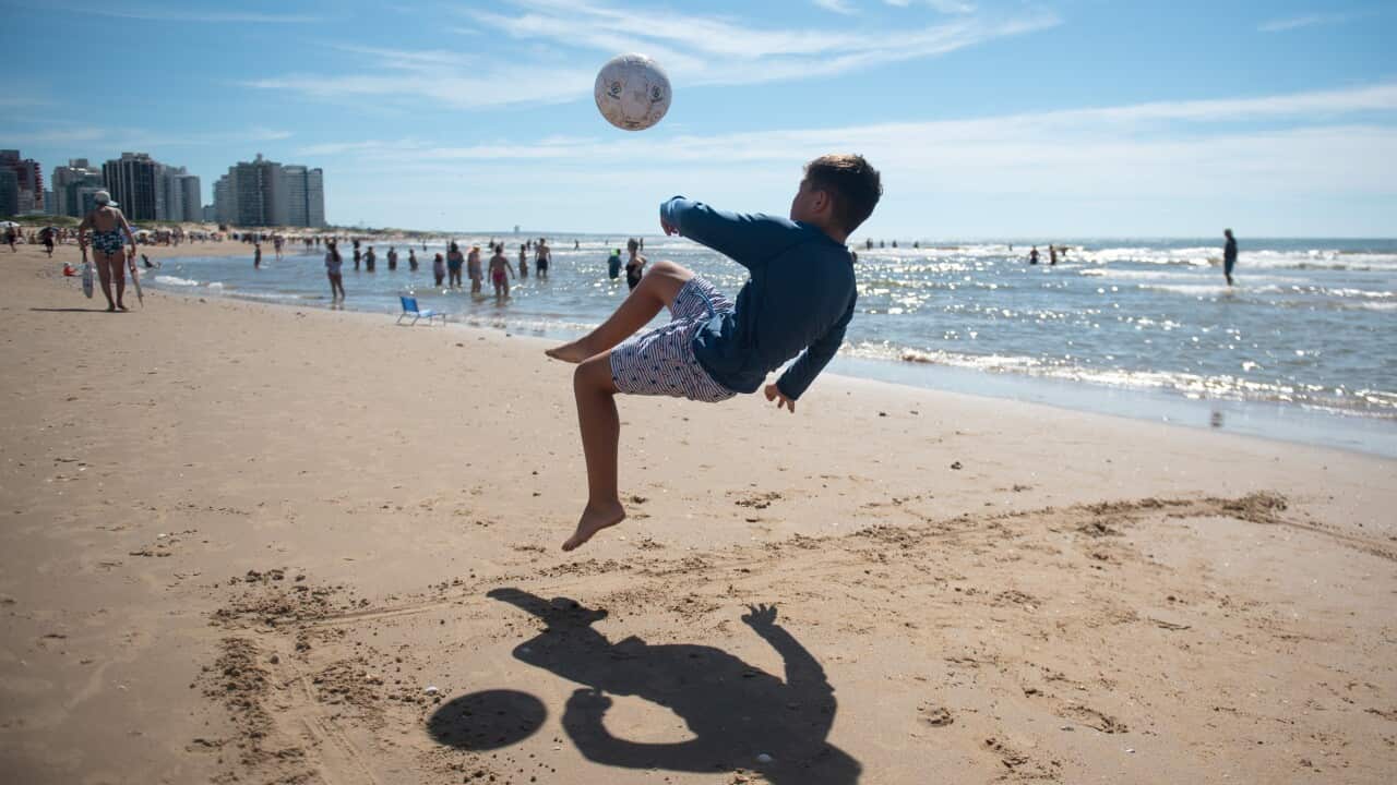 A boy playing football on a sunny day at a beach.