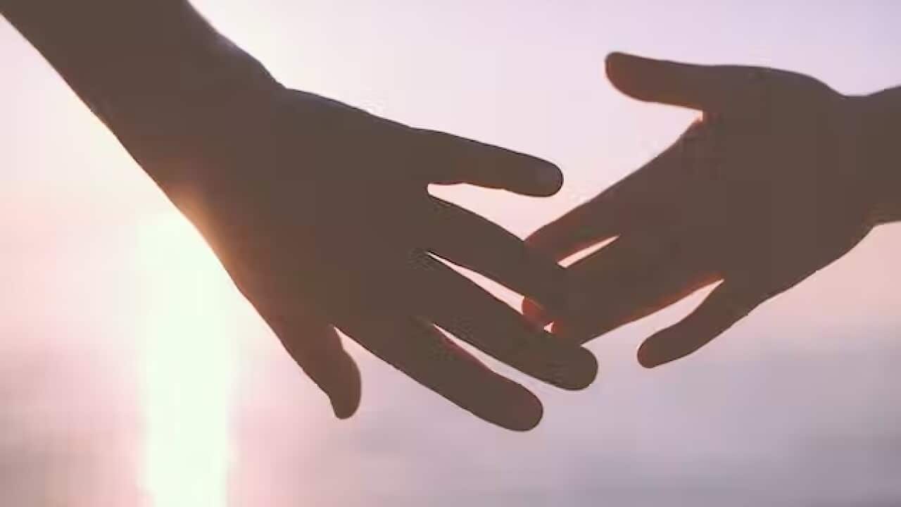 two backlit hands teaching out to hold each other against a pink sunset