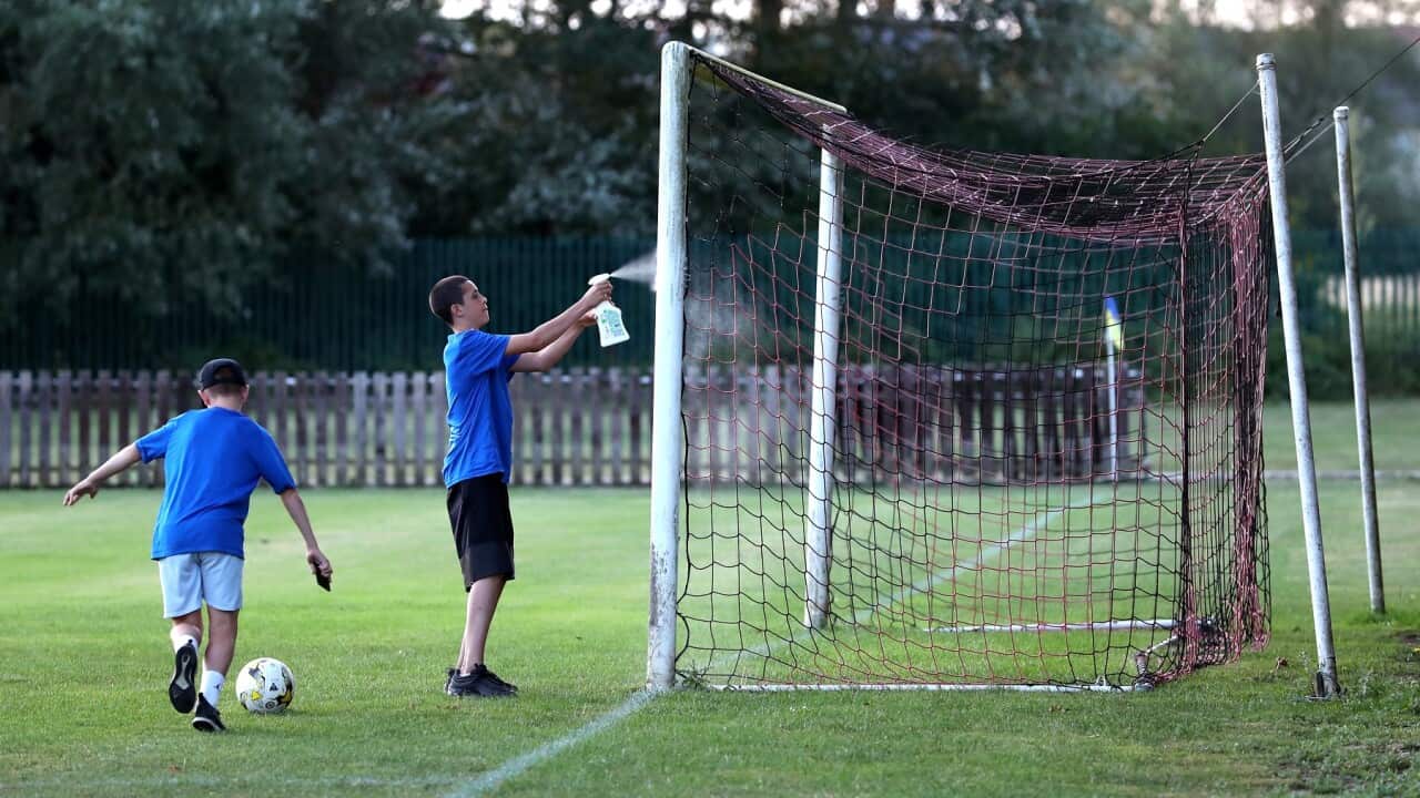 Ballboys spray disinfectant on the goalposts at a football pitch