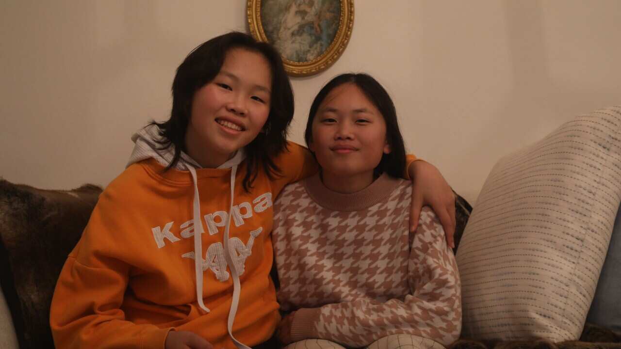 Jacqueline and her sister embrace on a couch smiling at the camera.
