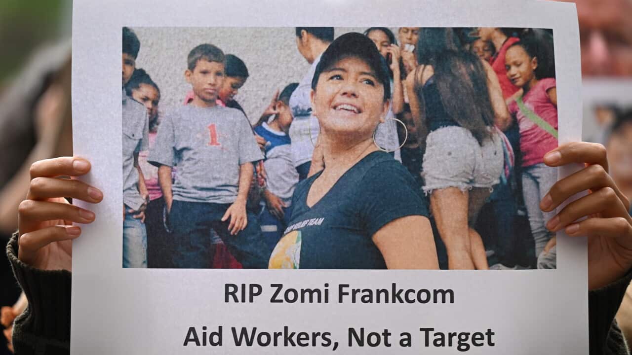 A person holding up a picture of a woman smiling, surrounded by children