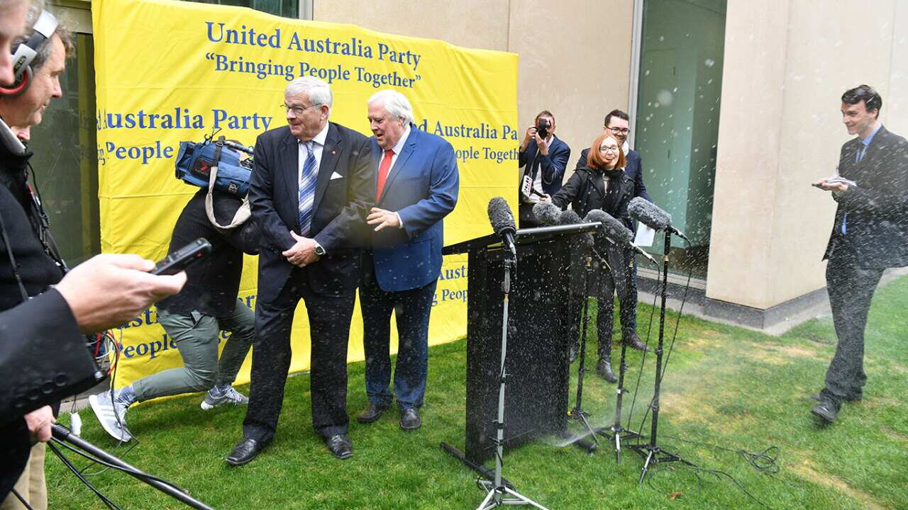 Former One Nation Senator Brian Burston and businessman Clive Palmer leave a press conference after a water sprinkler is turned on at Parliament House.