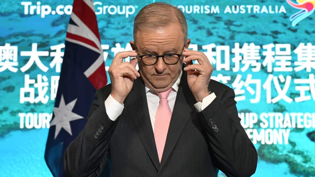 A man lifts his glasses awkwardly as he fronts a press conference