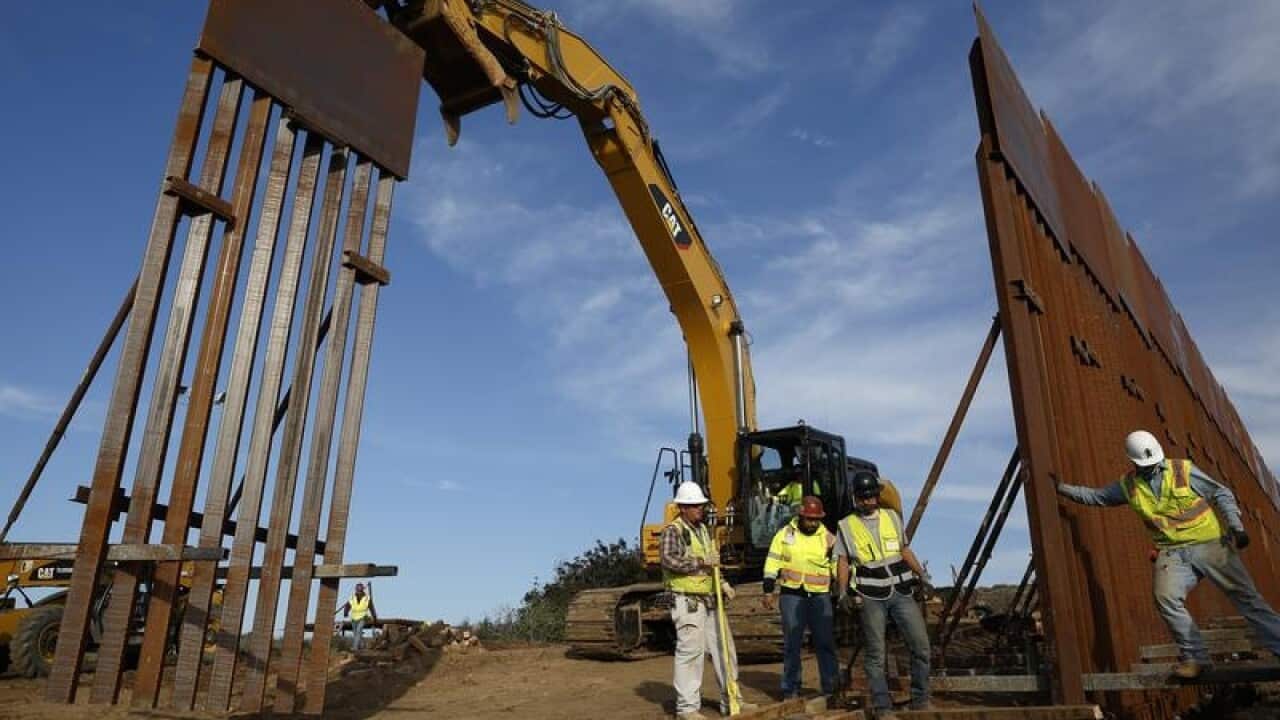 Construction crews install new border wall sections seen from Tijuana.