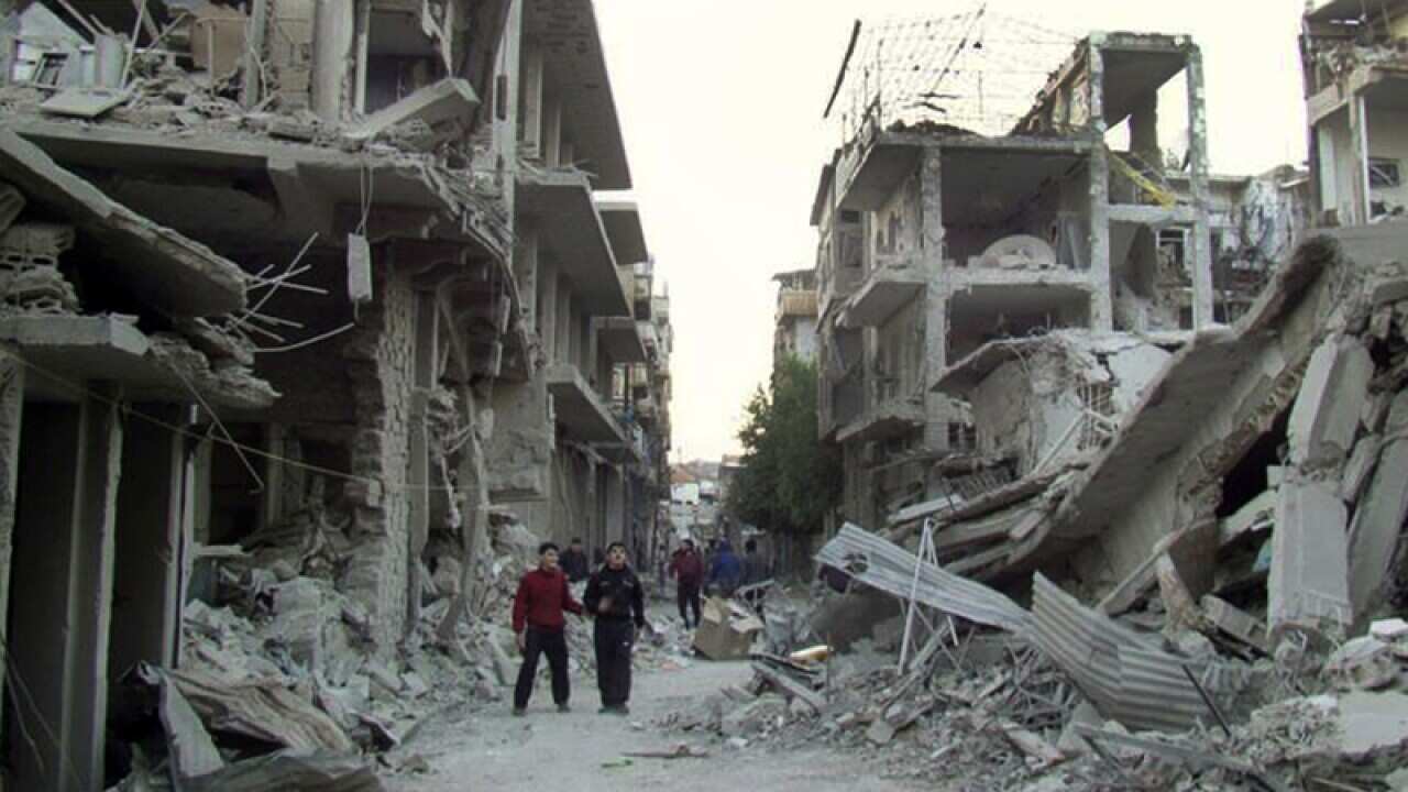 Syrian citizens walk in a destroyed area of Homs province