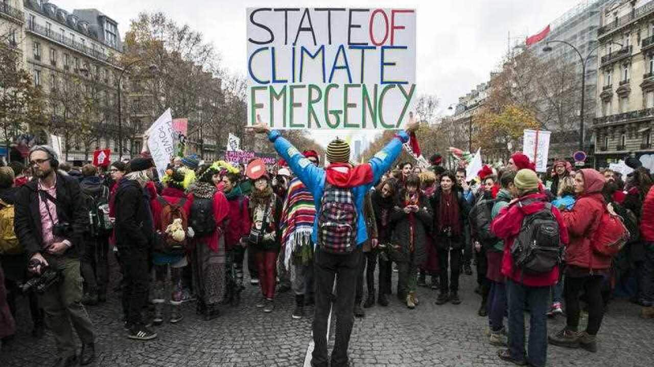 A demonstrator holds a poster stating 'State of Climate Emergency' behind Indigenous people during a protest during the COP21 in Paris, France, 2015