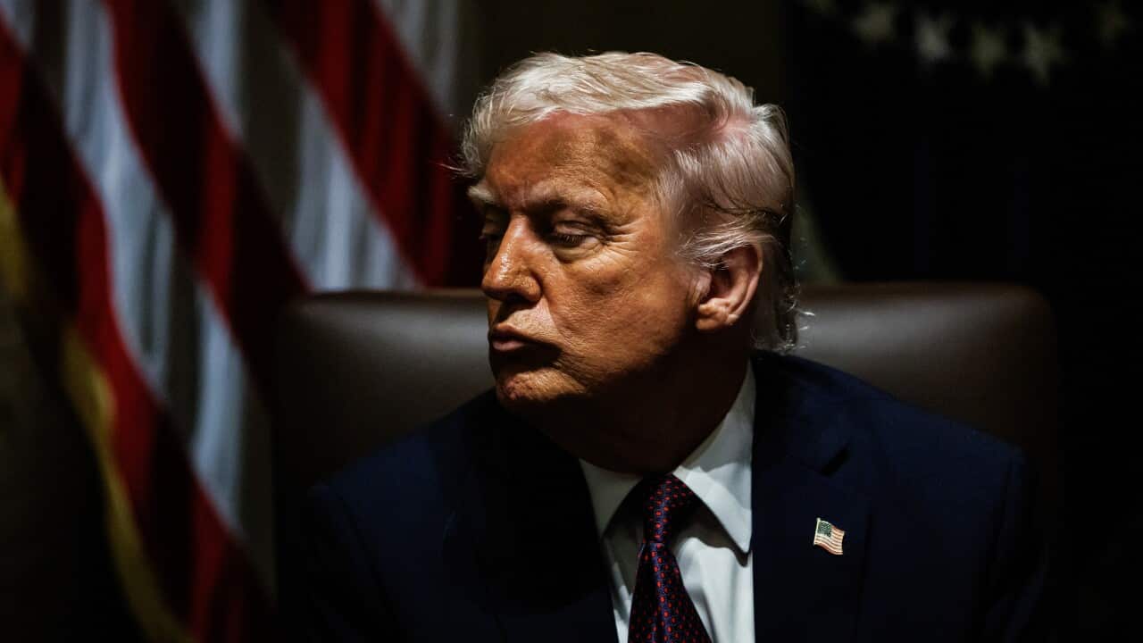 Donald Trump wearing a dark suit, white shirt, and a patterned tie. He has a serious expression and is looking to the side.