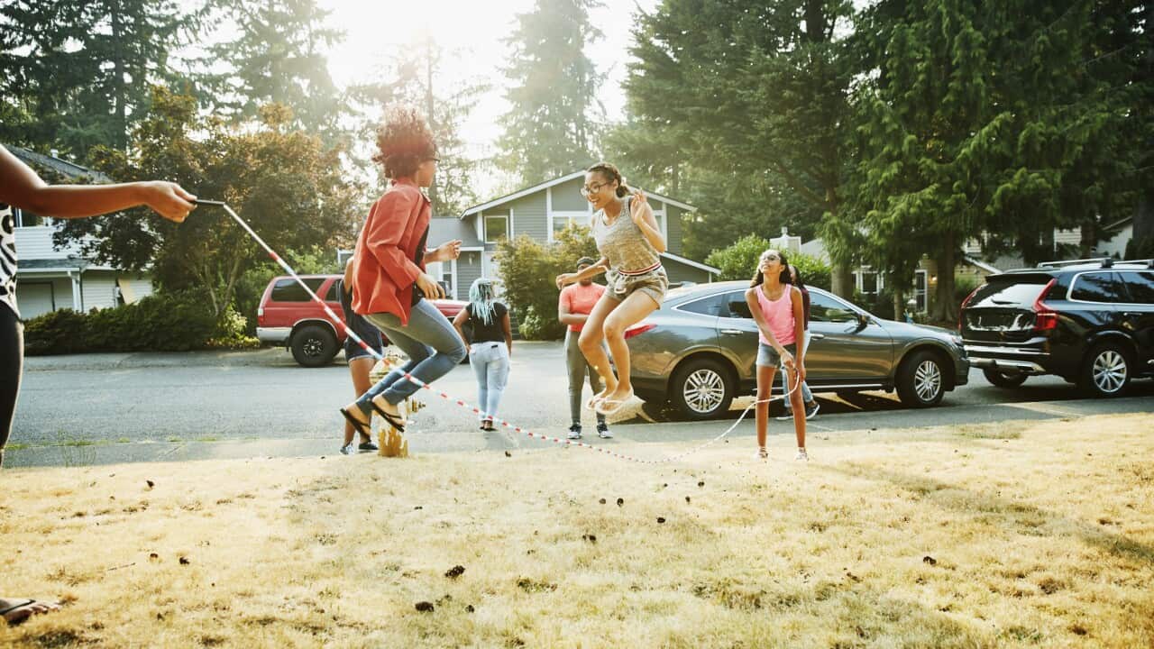 Group of teenage friends jumping rope together in front yard on summer evening