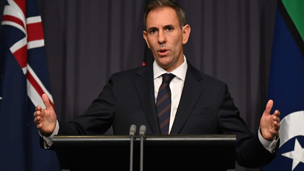 Treasurer Jim Chalmers talks to media from a podium flanked with Australian flags
