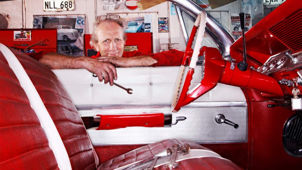 An older car mechanic working on a vintage car