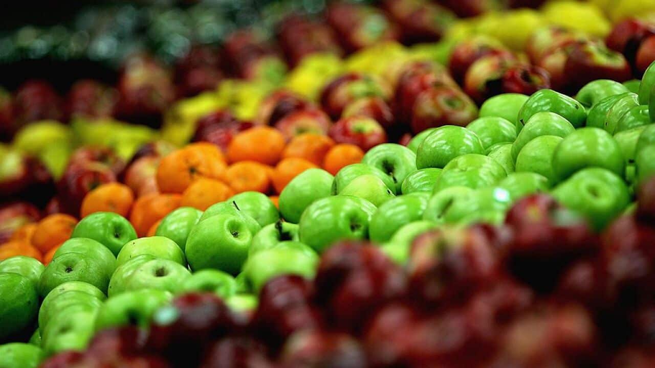 A supermarket shelf displays fresh fruit, including apples and oranges.