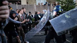 A group of white men faces off against police with riot shields in a suburban English street.