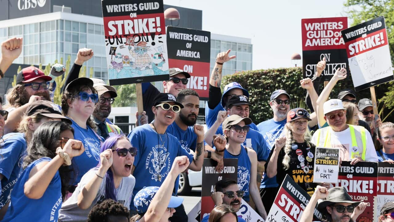 A group of people posing for a photo with their fists in the air. Some are holding placards that read "Writers Guild of America: On Strike!"