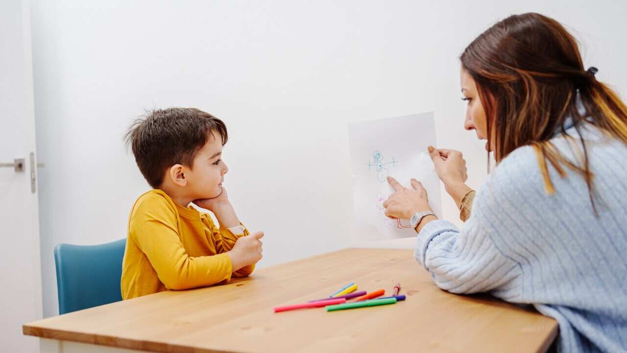 Psychology exercise for children, kid drawing family together with young educational therapist